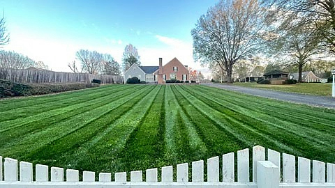 Mowing stripes across a front lawn behind a white picket fence