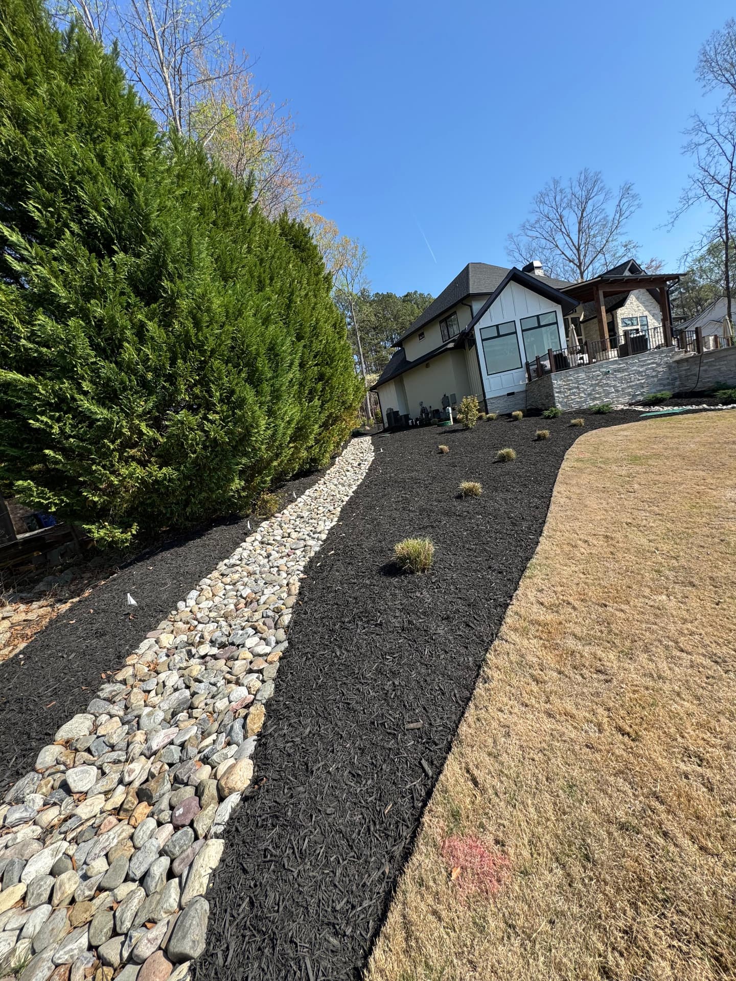 River rock drainage swale beside a mulched evergreen bed