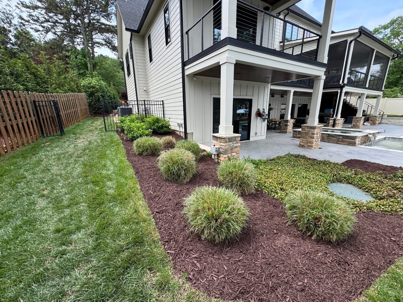 Rounded shrubs in a curved mulch bed beside a backyard porch