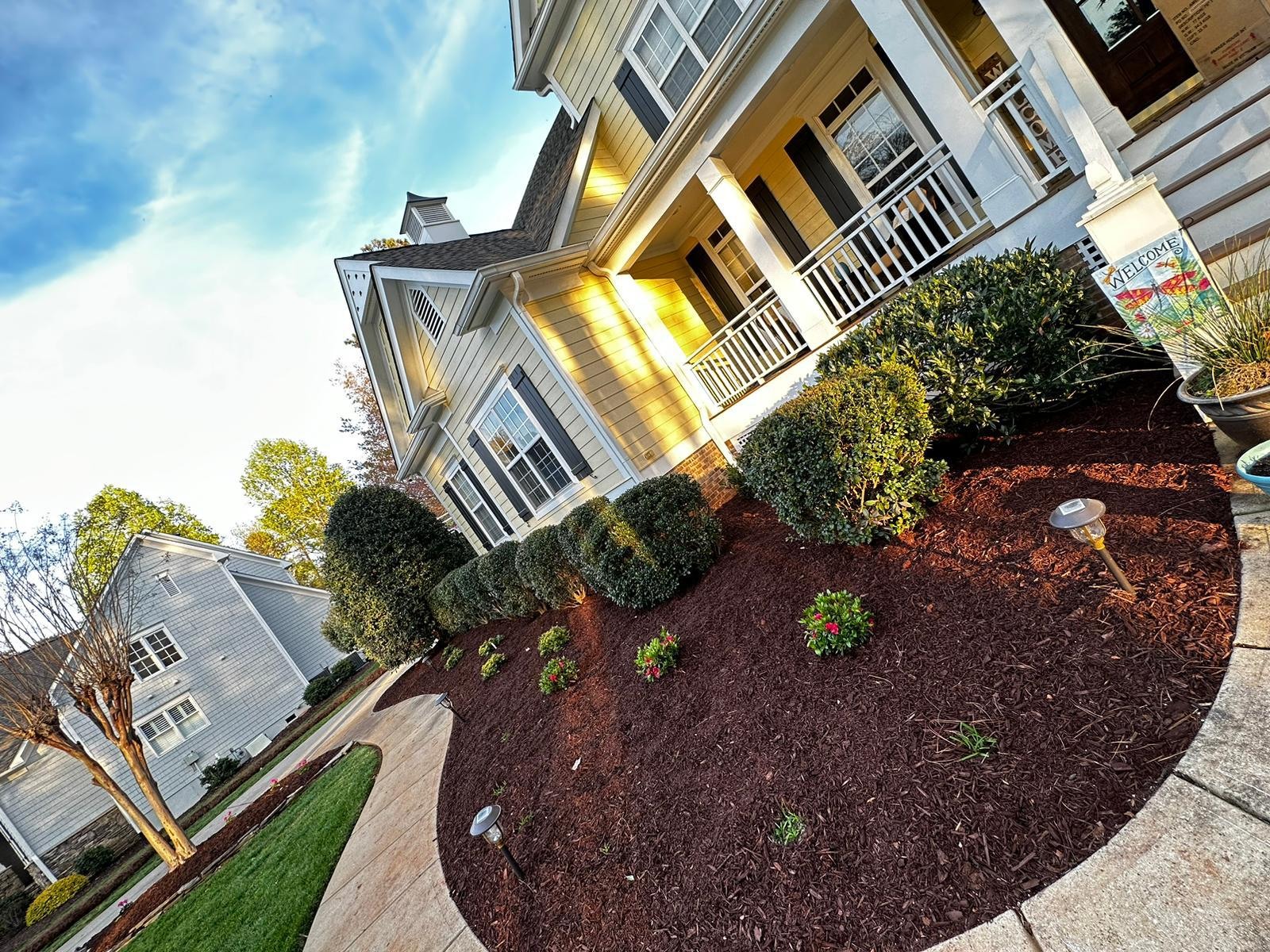 Flowering shrubs and fresh mulch beside a yellow home