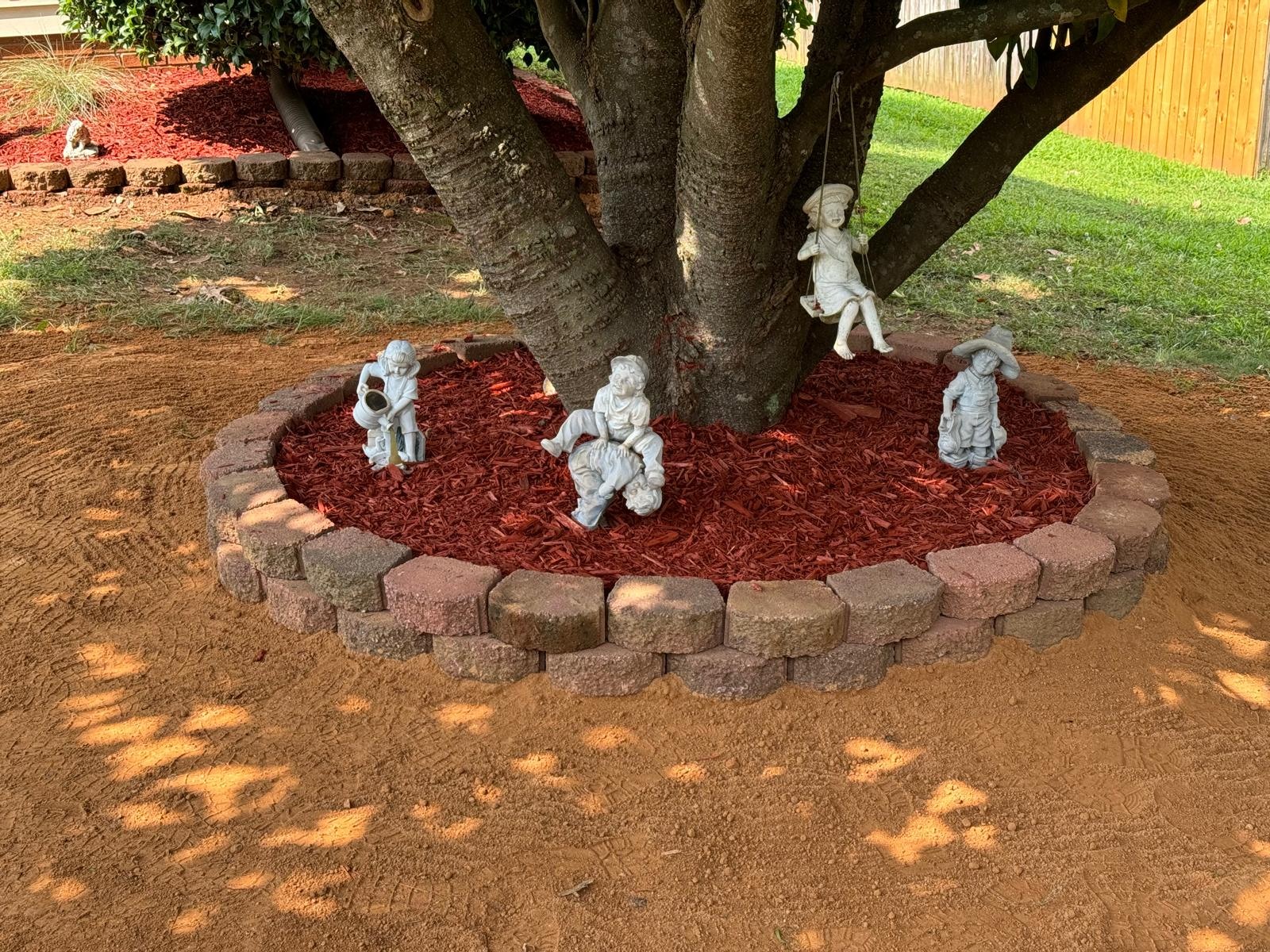 Red mulch and pale garden ornaments around a mature tree