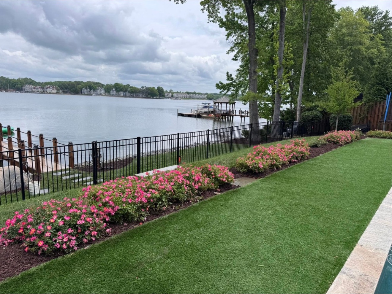 Lakeside lawn and pink flowering beds along a garden fence