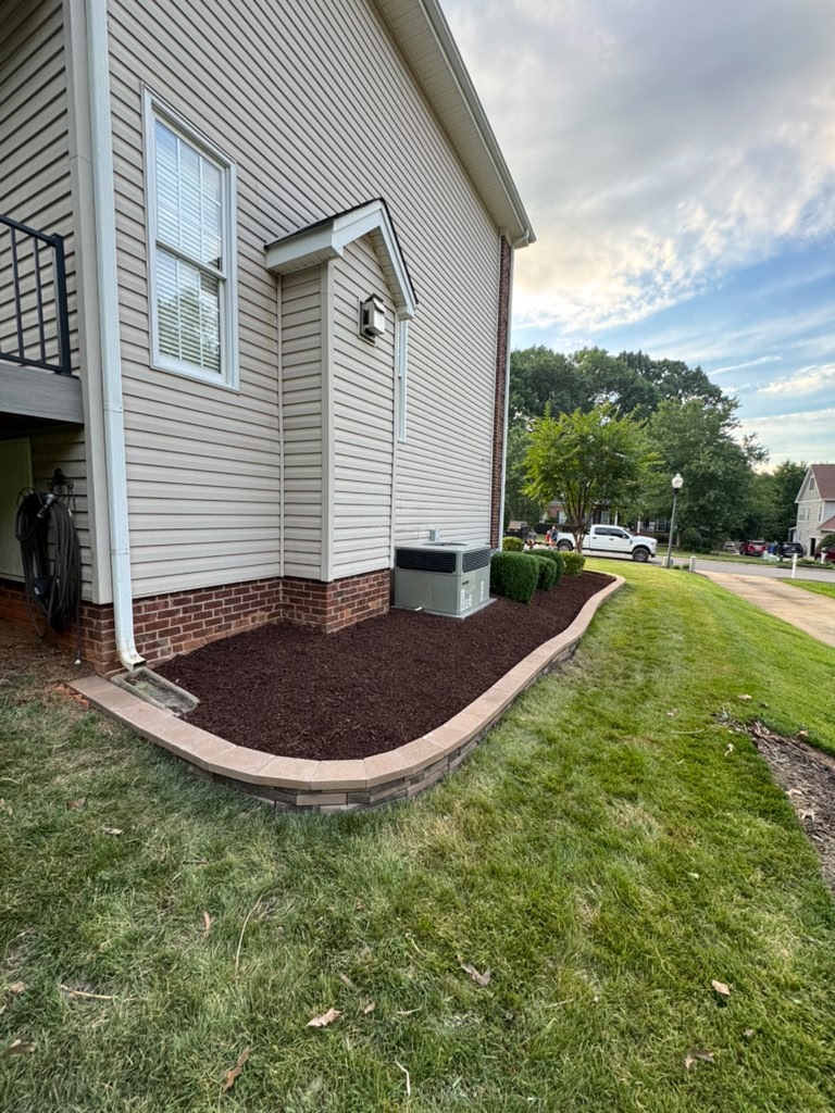 Stone-edged mulch bed along the side of a home