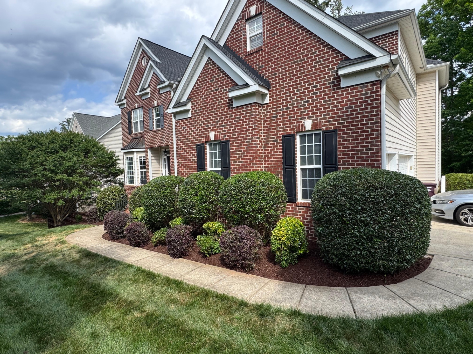 Shaped front shrubs and mulched beds at a brick home
