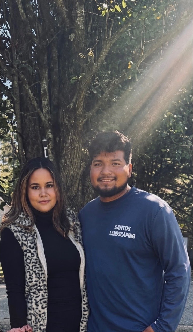 The owners of Santos Landscaping Pro LLC standing together beneath a large tree on a sunlit lawn