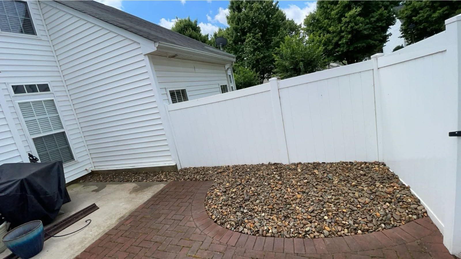 Mulch bed replaced with river rock beside a white fence