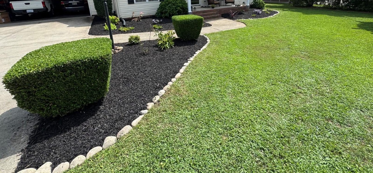 Clipped shrubs and stone-edged mulch beside a green lawn