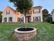 Circular raised stone tree bed set in a front lawn beside a home